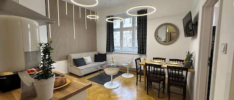 A modern kitchen with a dining area, wooden flooring, and pendant lighting.