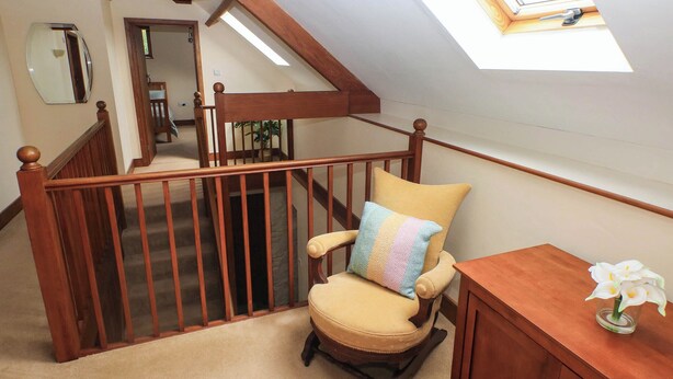 A wooden chair with a cushion in a room with a sloped ceiling and a wooden railing. - Penrhiwoli Barn (Llangammarch Wells)