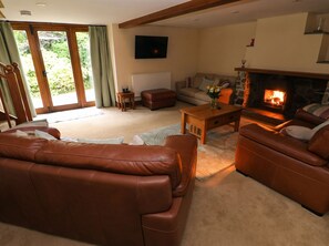 A living room with a fireplace, leather sofas, a coffee table, and a television. - Penrhiwoli Barn (Llangammarch Wells)
