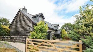 A wooden house with a stone facade, a gated entrance, and a surrounding garden. - Penrhiwoli Barn (Llangammarch Wells)