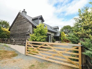 A wooden house with a stone facade, a gated entrance, and a surrounding garden. - Penrhiwoli Barn (Llangammarch Wells)