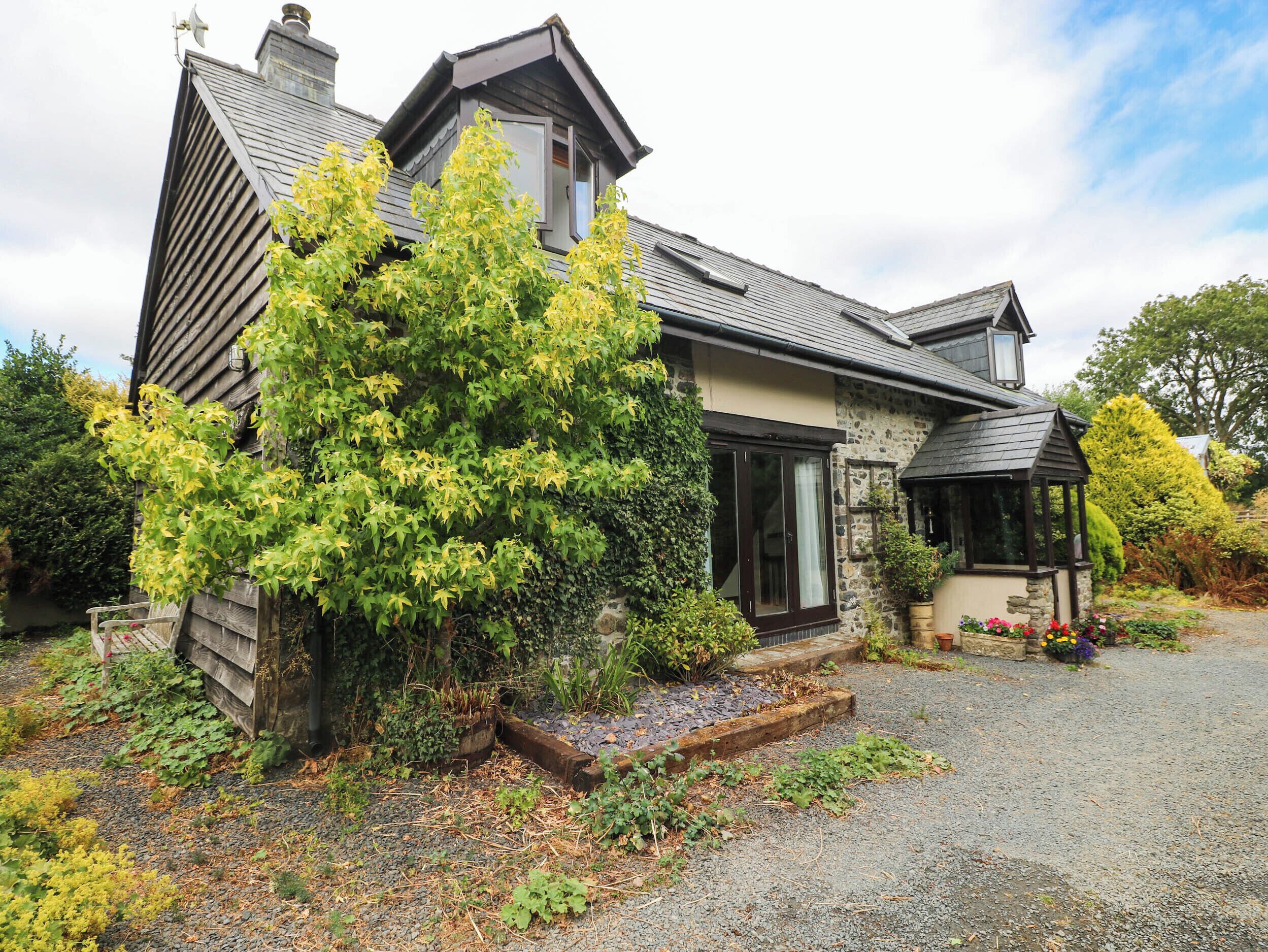 A two-story house with a stone facade, a wooden deck, and a small garden area with a variety of plants.