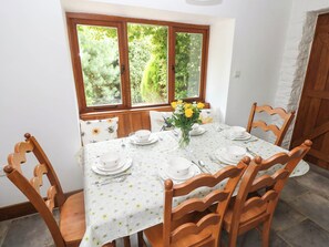 Mesa de comedor dispuesta para seis personas, con manteles florales, sillas de madera y un florero con flores amarillas.