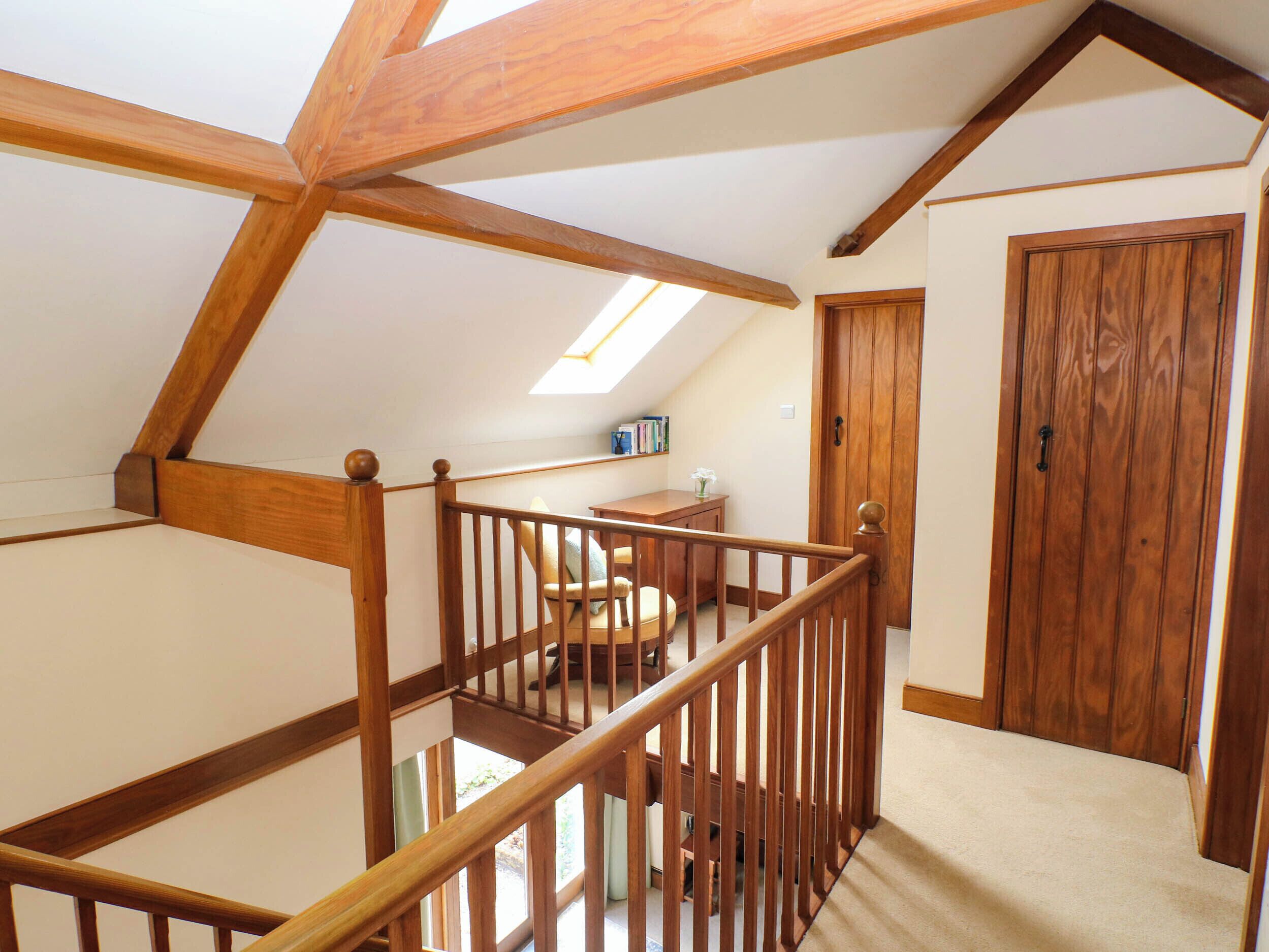 A wooden staircase with a railing leading to a room with a desk and chair, a wooden door, and a skylight.
