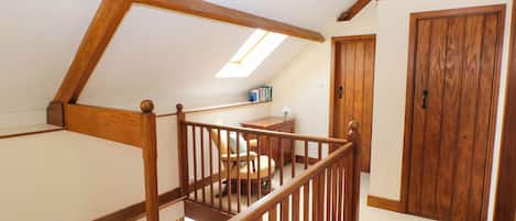 A wooden staircase with a railing leading to a room with a desk and chair, a wooden door, and a skylight.