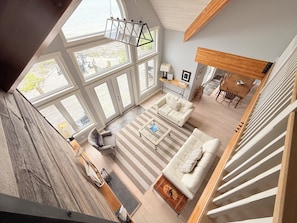 A spacious living area with a large window, a sofa, a coffee table, and a staircase. - Blue Baise - Tobermory Luxury Lakehouse (Tobermory)