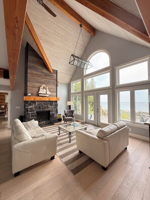A spacious living room with a fireplace, two sofas, and large windows overlooking a scenic view. - Blue Baise - Tobermory Luxury Lakehouse (Tobermory)