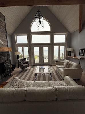 A spacious living room with a large window overlooking a body of water, a fireplace, and a high ceiling. - Blue Baise - Tobermory Luxury Lakehouse (Tobermory)