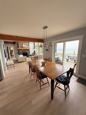 A spacious dining area with a wooden table and chairs, a fireplace, and a view of the beach. - Blue Baise - Tobermory Luxury Lakehouse (Tobermory)