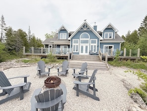 A two-story house with a deck, outdoor seating area with Adirondack chairs, and a fire pit. - Blue Baise - Tobermory Luxury Lakehouse (Tobermory)