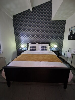Un letto con testiera, due lampade ai comodini e una parete decorata.