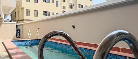 A swimming pool with a metal handrail, a tiled edge, and a building in the background.