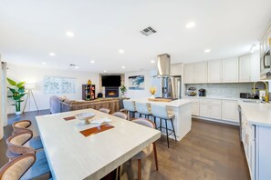 A modern kitchen with white cabinetry, a central island, and a dining area with a long table and chairs. - Pacific Grand - Dual Living Near Mission Bay (San Diego)