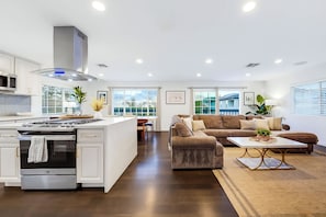 Een moderne keuken met een centraal eiland, een eethoek met een bruine bank en een woonkamer met een salontafel.