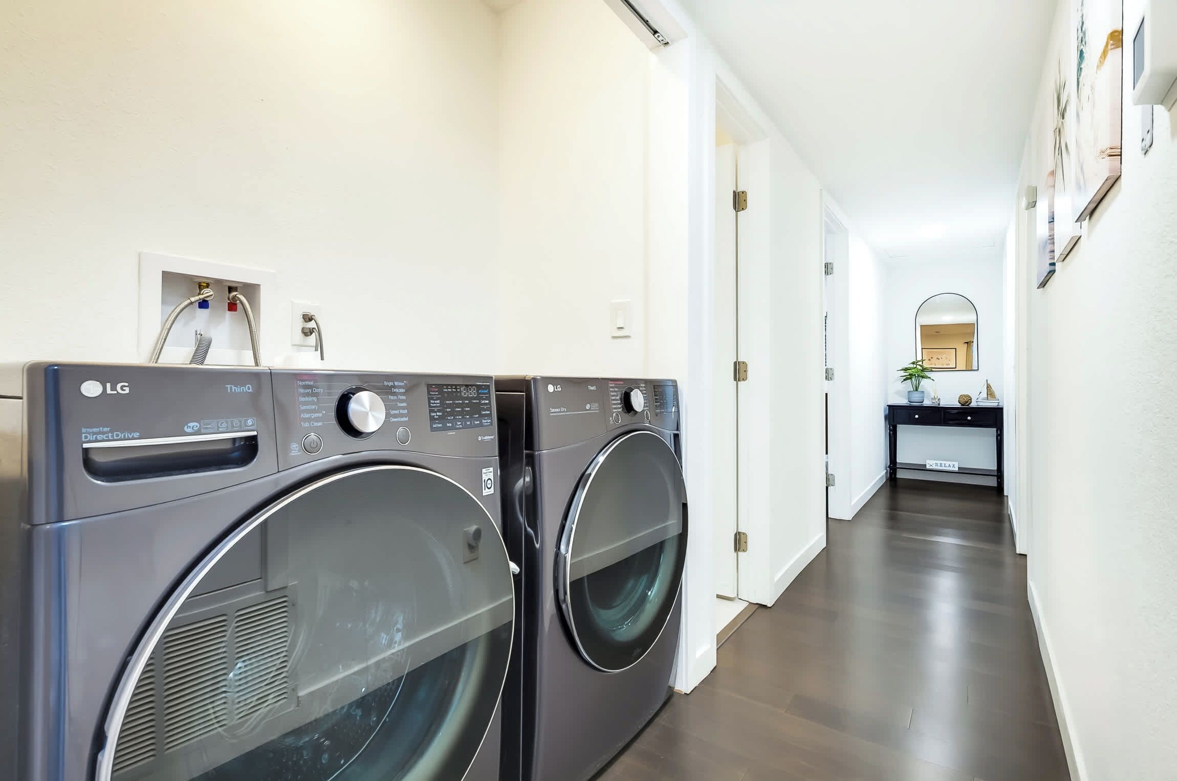Un área de lavandería con dos lavadoras LG ThinQ Direct Drive, un lavamanos pequeño y un espejo en la pared.