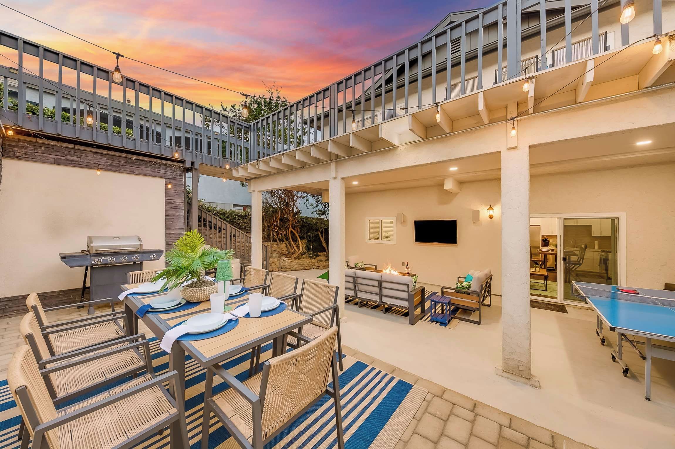A covered outdoor patio with a barbecue, seating area, and a ping pong table.