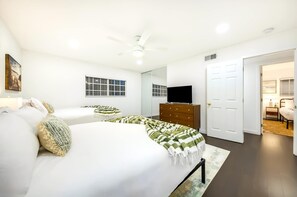 A bedroom with a bed, a dresser, a television, a mirror, and a door leading to another room. - Pacific Grand - Dual Living Near Mission Bay (San Diego)