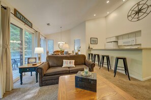Una sala de estar con un sofá, una mesa de centro, una lámpara y vistas al exterior.