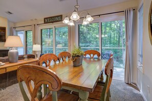 A dining area with a wooden table, chairs, a potted plant, and a 'WELCOME' sign. - Dreams and Streams at Pinebrook- Your Perfect Northern Michigan Escape! (Bellaire)