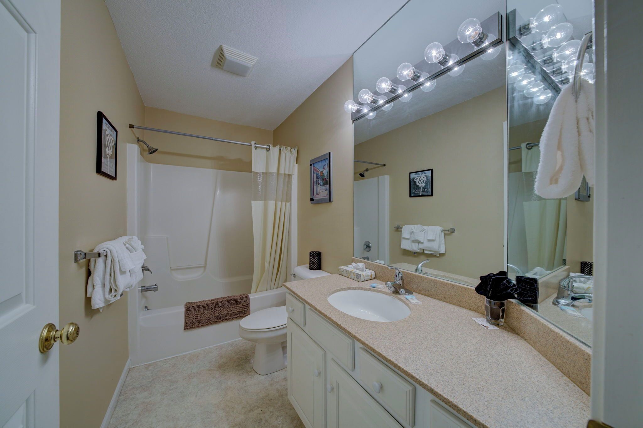 A bathroom with a bathtub, toilet, vanity with a sink, and a large mirror with lights.