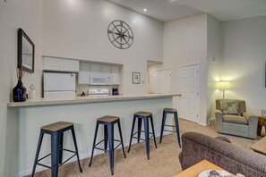 A modern kitchen with white cabinets, a central island with stools, and a compass wall decoration. - Dreams and Streams at Pinebrook- Your Perfect Northern Michigan Escape! (Bellaire)