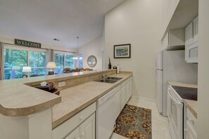 A modern kitchen with a curved countertop, built-in dishwasher, and a view of the outdoors through large windows. - Dreams and Streams at Pinebrook- Your Perfect Northern Michigan Escape! (Bellaire)
