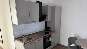 Een moderne keuken met een ingebouwde oven, een spoelbak en een fornuis. Er staat een eettafel met stoelen.