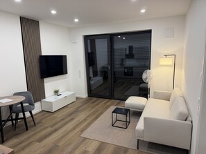 Ein modernes Wohnzimmer mit Flachbildfernseher, einer Couch, einem Couchtisch, einem Essbereich mit Stühlen und einer Glastür zum Außenbereich.
