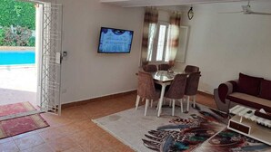 A living room with a dining area, a television mounted on the wall, a ceiling fan, and a view of the outside. - Villa Cranzy: 3BR with private pool, bianki, AL agami, Alexandria ,Egypt (Alexandria Governorate)