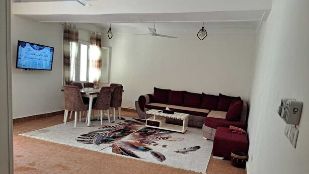 A living room with a sofa, a dining table with chairs, a television mounted on the wall, and a ceiling fan. - Villa Cranzy: 3BR with private pool, bianki, AL agami, Alexandria ,Egypt (Alexandria Governorate)