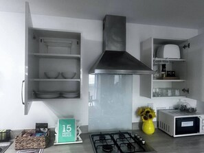 Une cuisine équipée d’une cuisinière à gaz, d’une hotte en acier inoxydable et de placards ouverts contenant de la vaisselle et des bols.