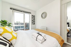 A bedroom with a bed, a window, a radiator, and a wall clock. - Stylish 1-bed flat | Free parking | Fast Wi-Fi (Basingstoke)