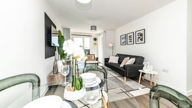 A modern living room with a sofa, a dining table set for four, and a TV mounted on the wall. - Stylish 1-bed flat | Free parking | Fast Wi-Fi (Basingstoke)
