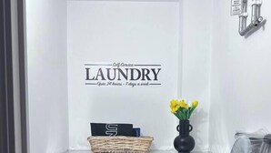 A laundry area with a washing machine, a shelf with a basket and a vase of flowers, and a wall-mounted faucet. - Stylish 1-bed flat | Free parking | Fast Wi-Fi (Basingstoke)