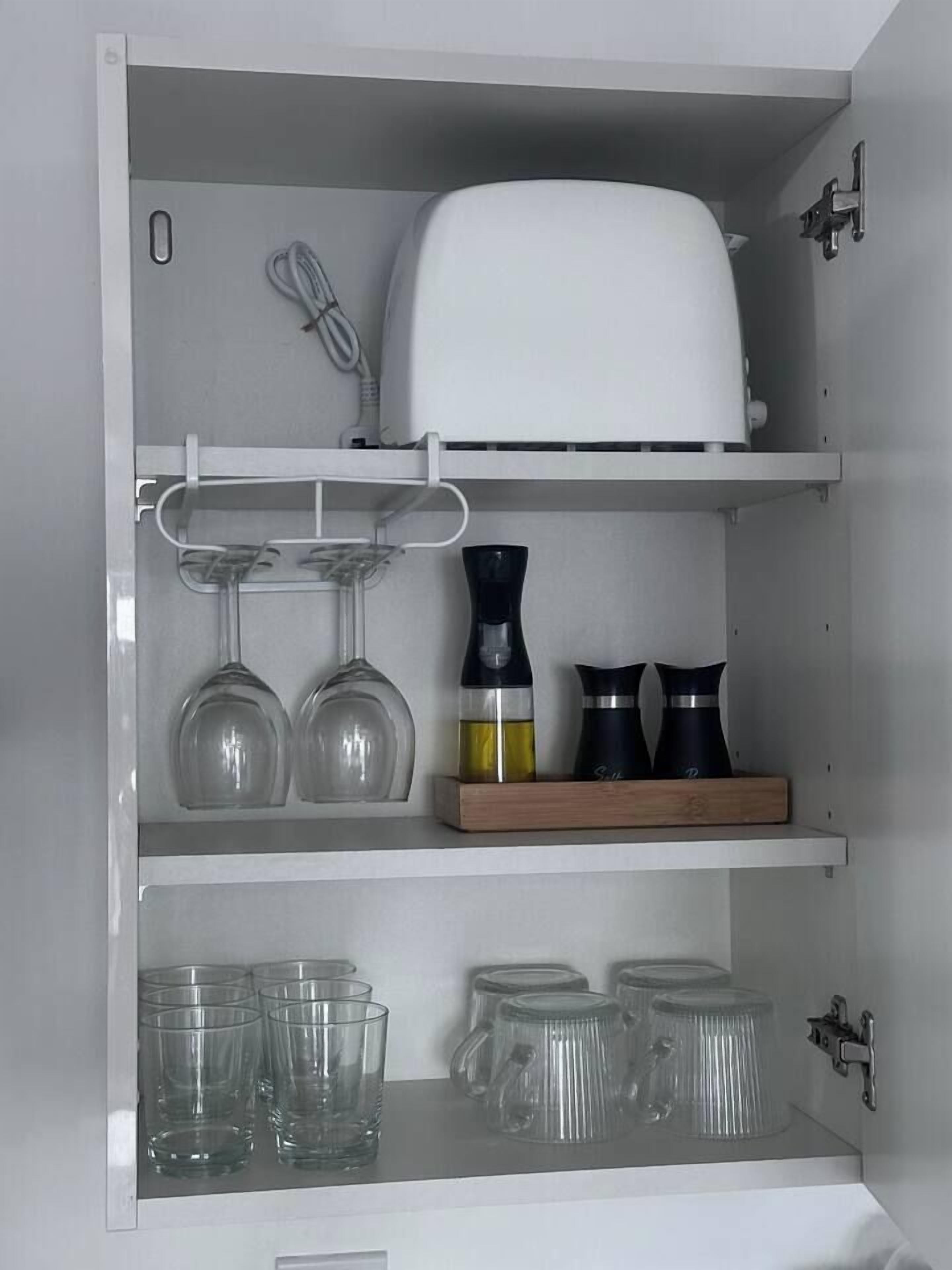 Un mueble de cocina con un electrodoméstico blanco, copas de vino y recipientes de vidrio transparentes.
