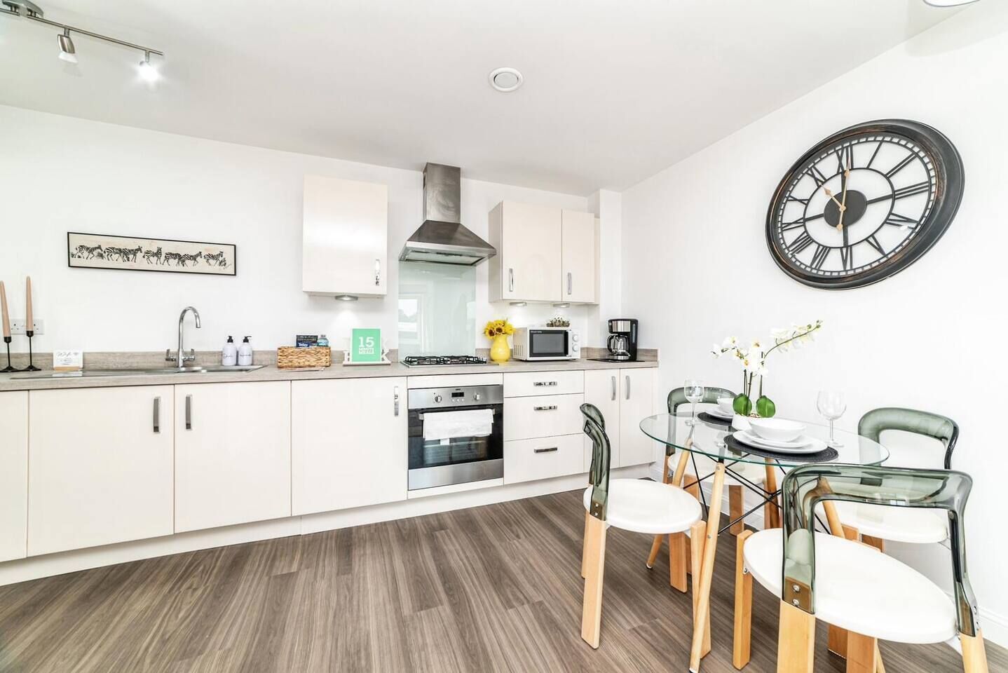 A modern kitchen with white cabinets, a stainless steel range hood, and a dining area with a glass table and chairs.