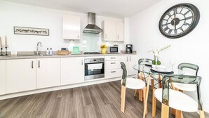 A modern kitchen with white cabinets, a stainless steel range hood, and a dining area with a glass table and chairs. - Stylish 1-bed flat | Free parking | Fast Wi-Fi (Basingstoke)