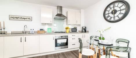 A modern kitchen with white cabinets, a stainless steel range hood, and a dining area with a glass table and chairs.