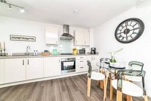 A modern kitchen with white cabinets, a stainless steel range hood, and a dining area with a glass table and chairs. - Stylish 1-bed flat | Free parking | Fast Wi-Fi (Basingstoke)