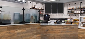 Een moderne bar met een houten toonbank, planken met flessen en een koffieapparaat.