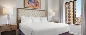 Een hotelkamer met een groot bed, twee nachtkastjes, een hoofdbord en een raam met uitzicht op gebouwen.