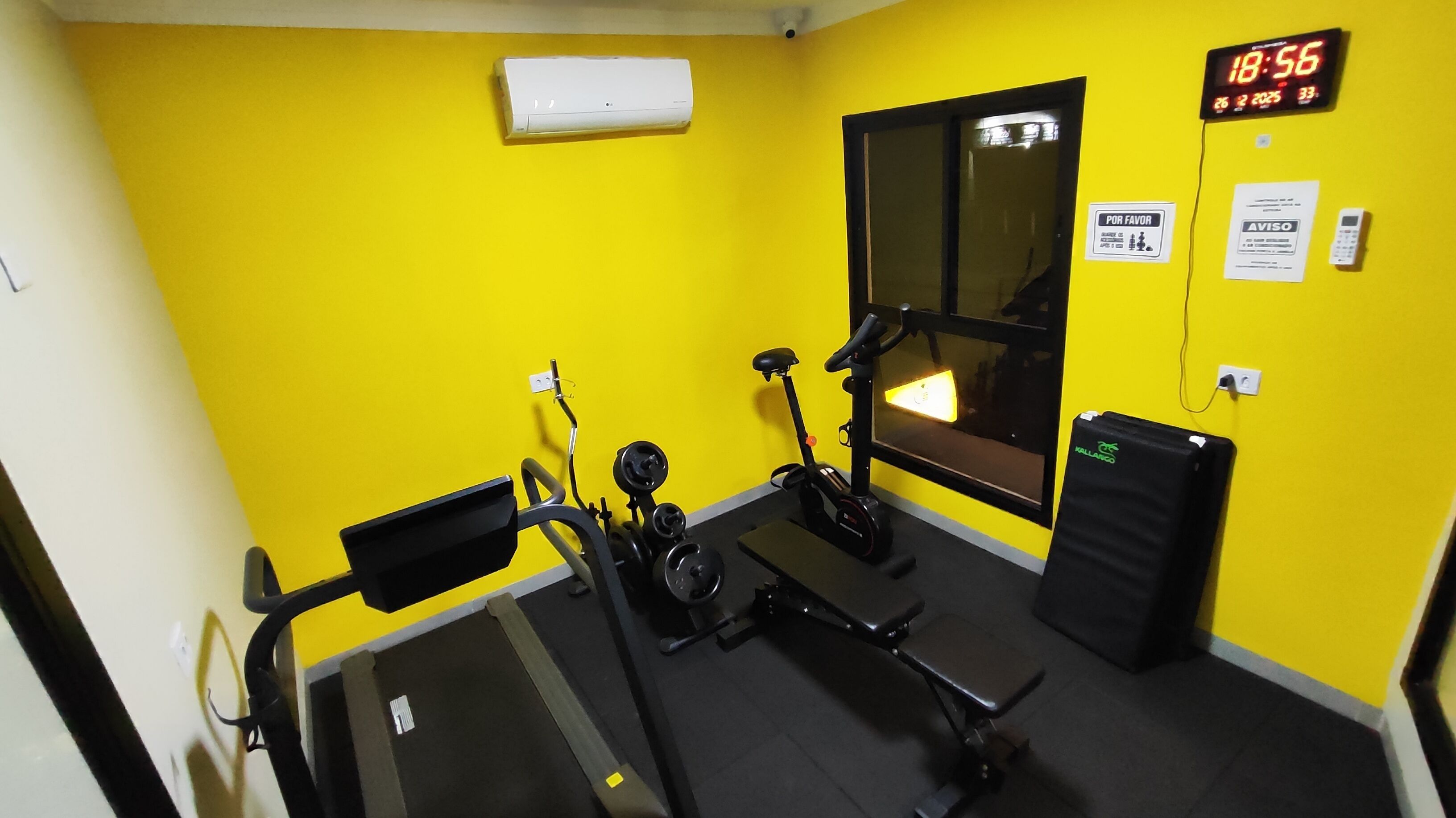 Un gimnasio con equipo de ejercicio, un reloj digital y una ventana.