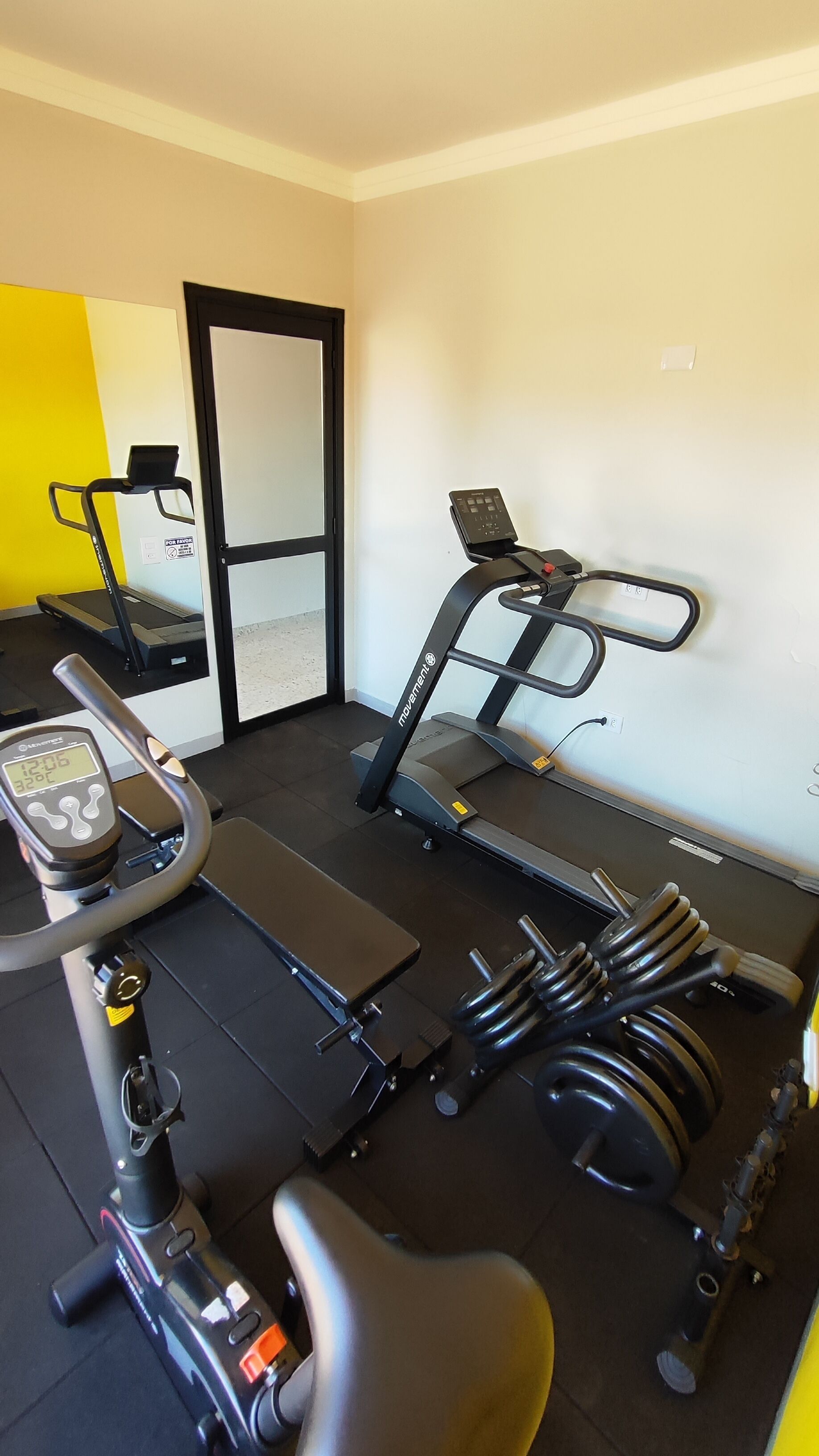 Un gimnasio con equipo de ejercicio, incluyendo una cinta de correr, bicicleta estática y pesas.