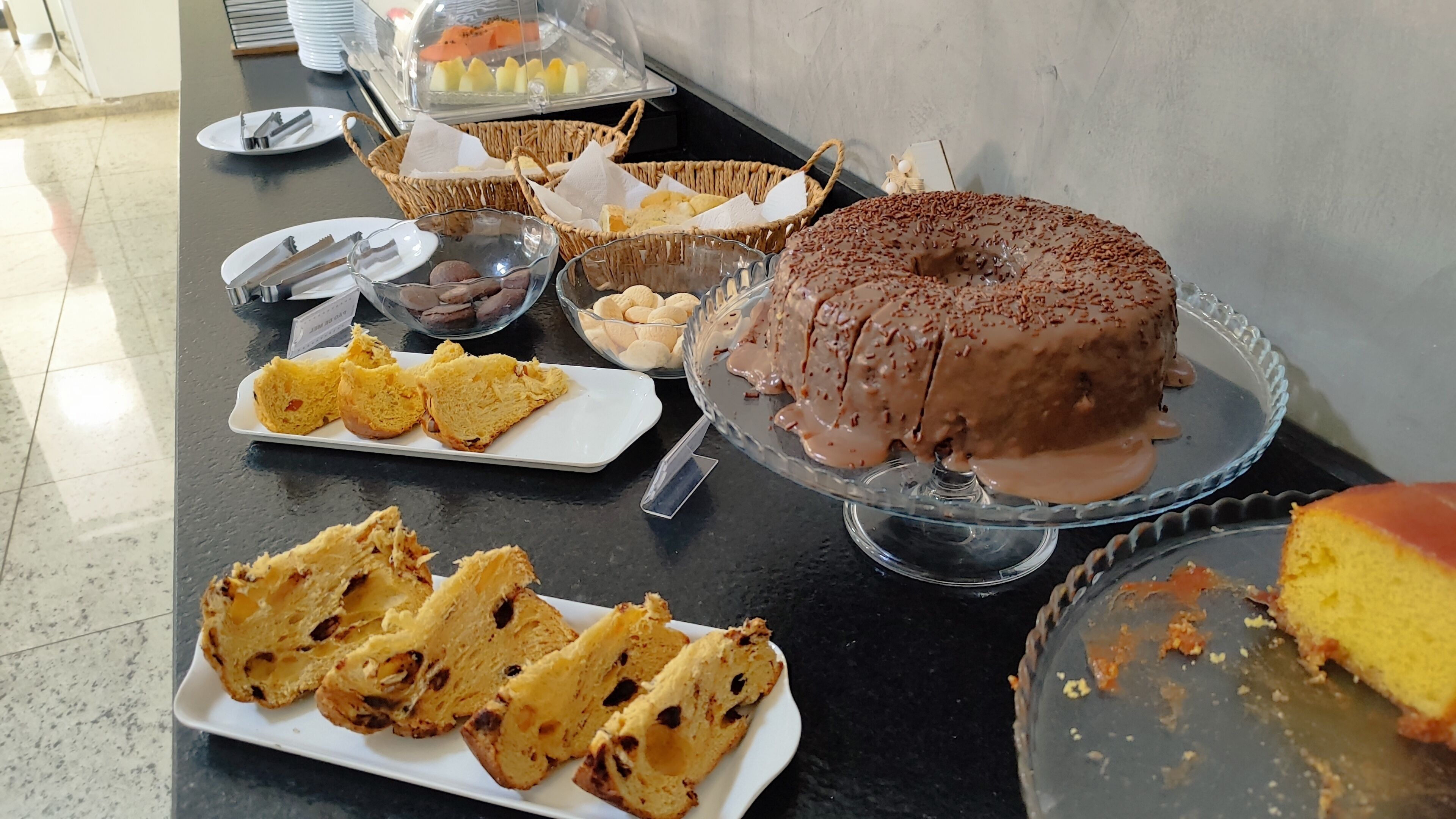 Una mesa de buffet con diferentes alimentos, incluyendo pastel de chocolate, pan y bollería.