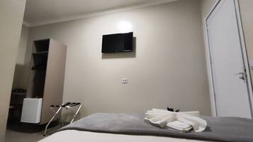 A hotel room with a bed, a television mounted on the wall, a wardrobe, and a small table with a towel.