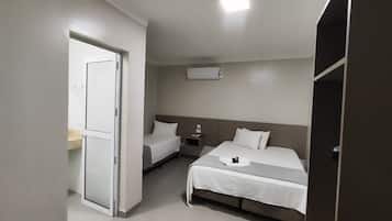 Et hotelværelse med to senge, et natbord, en vægmonteret aircondition og en dør til et andet rum.