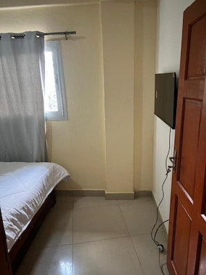 A bedroom with a bed, a window with curtains, a television mounted on the wall, and a wooden door. - Luxury and Classy with City View (Yaoundé)