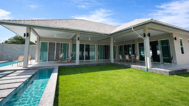 Ein modernes Haus mit Schwimmbad, überdachter Terrasse und gepflegtem Rasen.