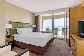 Ein Hotelzimmer mit einem großen Bett, einem Fernseher, einem Schreibtisch und einem Balkon mit Blick.