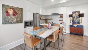 A modern kitchen with white cabinets, a marble island, and a dining area with leather chairs. - DeLuna Vista the Brent Lofts (Pensacola)